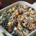a mixture of pasta with ground meat, bacon, diced apple, and spinach topped with melted cheese in a baking dish
