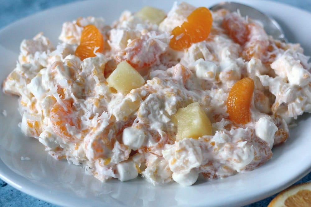a mixture of mandarin oranges, pineapple chunks, and marshmallows in a creamy coconut sauce
