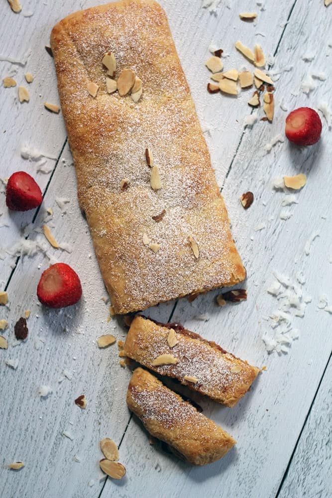 a rectangle-shaped strudel garnished with sliced, chopped almonds on a whitewashed wood surface