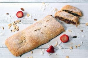 a flat rectangular shaped pastry filled with a glazed brown mixture on a wood surface