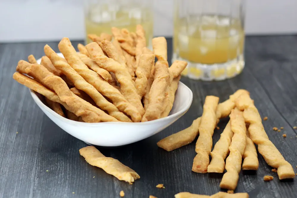 a white bowl filled with twisted baked cheese straws on a wooden surface