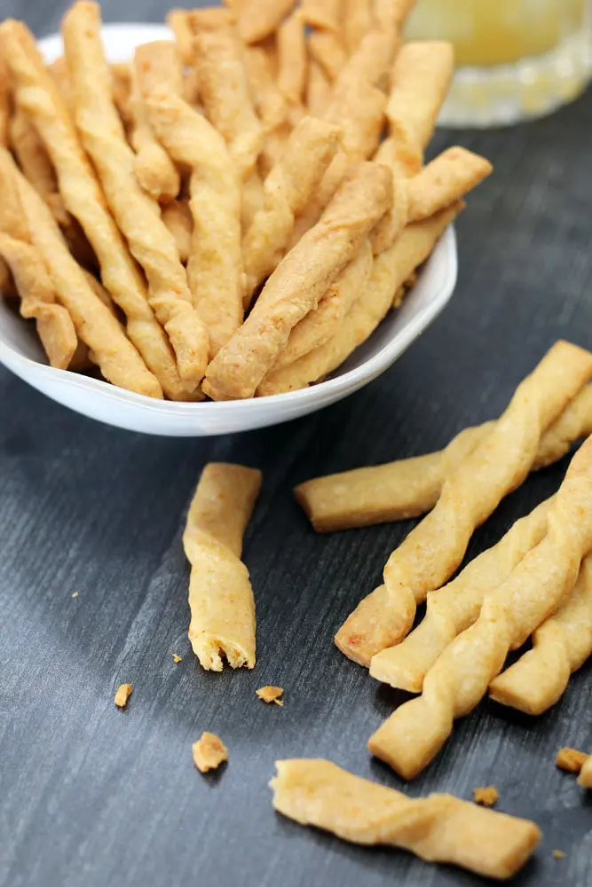 a white bowl filled with twisted baked cheese straws on a wooden surface