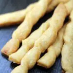 a pile of twisted golden brown baked bread stick style pastries on a wood surface