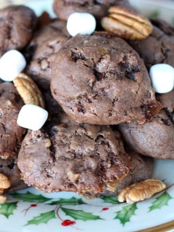chocolate cookies on a christmas patterned plate garnished with marshmallows and pecans