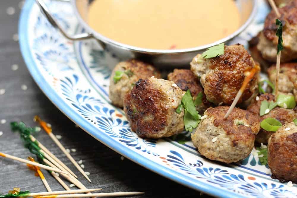 Pork and Mushroom Meatballs garnished with chopped green herbs with a metal bowl filled with an opaque orange sauce