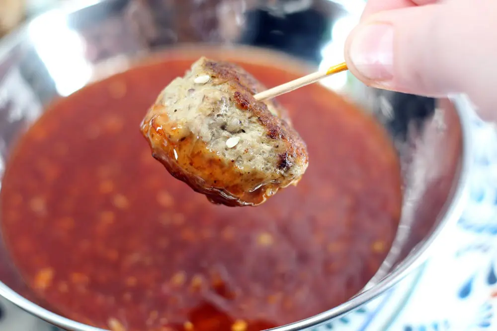a hand holding a meatball dipped in a red sauce and skewered with a toothpick