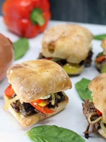 four Crock-Pot Italian Beef Sandwiches on a white platter garnished with whole basil leaves