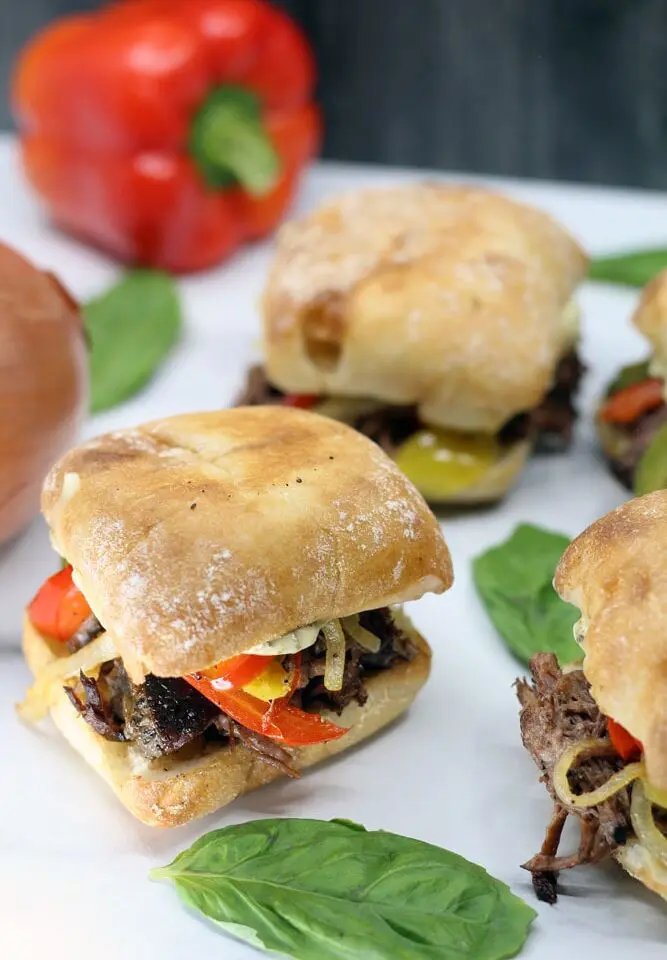 four Crock-Pot Italian Beef Sandwiches on a white platter garnished with whole basil leaves
