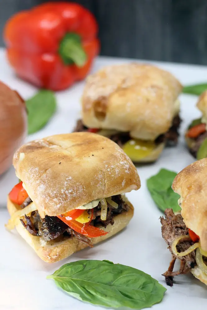 four Crock-Pot Italian Beef Sandwiches on a white platter garnished with whole basil leaves