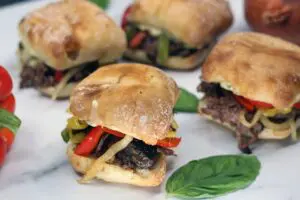 beef sandwiches topped with cooked sliced vegetables on browned buns