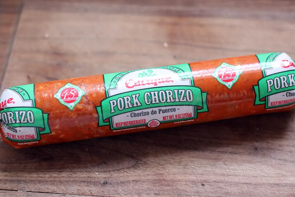 a tube of Cacique premade chorizo that is used in the refried beans recipe sitting on a wooden cutting board