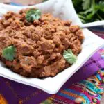brown refried Beans with Chorizo garnished with cilantro leaves in a star shaped white bowl sitting on colorful Mexican-style linens