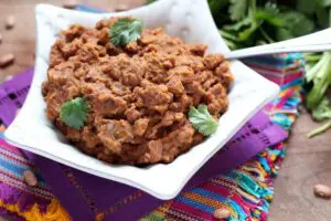 brown refried Beans with Chorizo garnished with cilantro leaves in a star shaped white bowl sitting on colorful Mexican-style linens