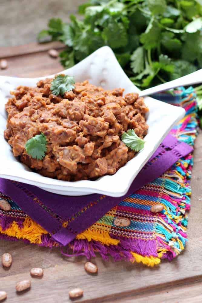 Refried Beans with Chorizo garnished with cilantro leaves in a star shaped white bowl sitting on colorful Mexican-style linens with a cilantro bunch in the background