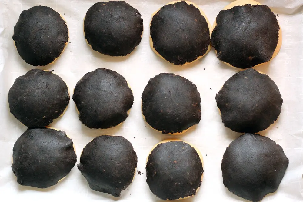 concha dough balls after topping with the chocolate dough sitting on a sheet pan lined with parchment paper