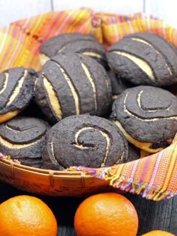 Chocolate Conchas or Mexican Sweet Bread flavored with chocolate and orange in a woven basket lined with a colorful Mexican style linen and surrounded by fresh oranges