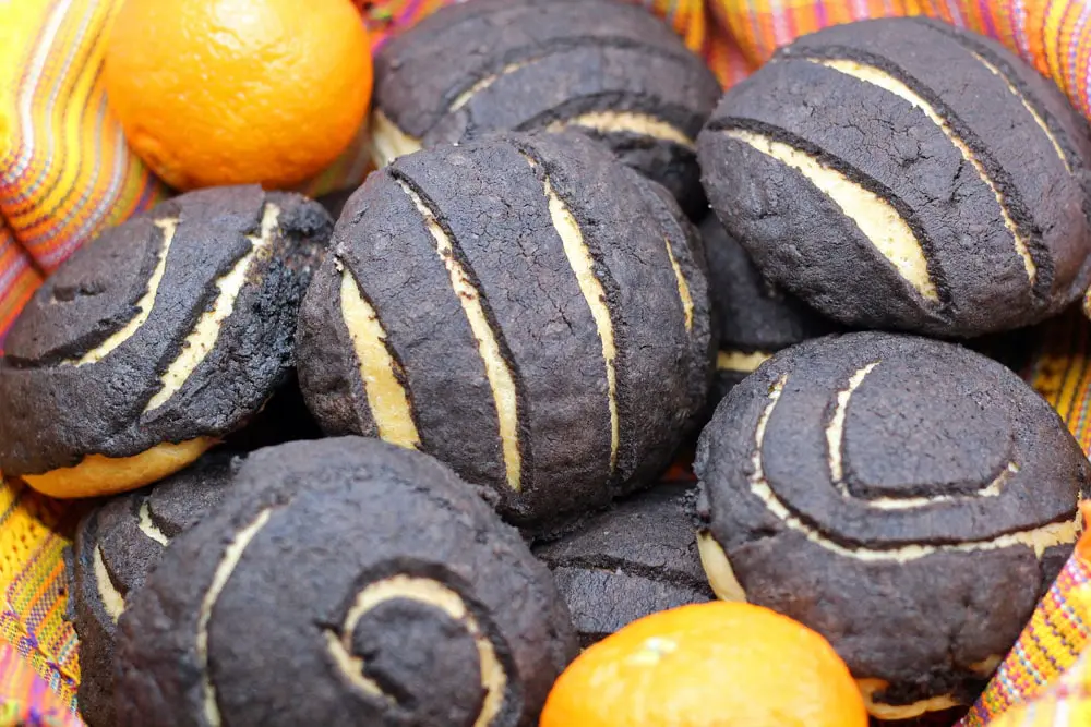 Chocolate Conchas or Mexican Sweet Bread flavored with chocolate and orange in a woven basket lined with a colorful Mexican style linen and surrounded by fresh oranges