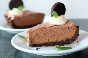 a slice of Thin Mint No-Bake Chocolate Cheesecake in a red pie pan garnished with whipped cream, green sprinkles and whole thin mint cookie
