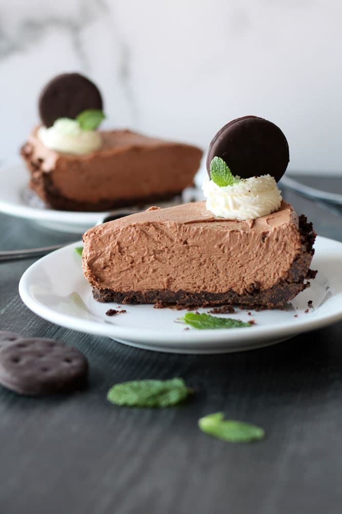 a slice of Thin Mint No-Bake Chocolate Cheesecake in a red pie pan garnished with whipped cream, green sprinkles and whole thin mint cookie