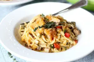 a bowl of Chicken Spaghetti or spaghetti noodles covered in a mushroom cream sauce with chicken, onions and peppers and topped with melted cheddar, breadcrumbs, and crispy jalapenos