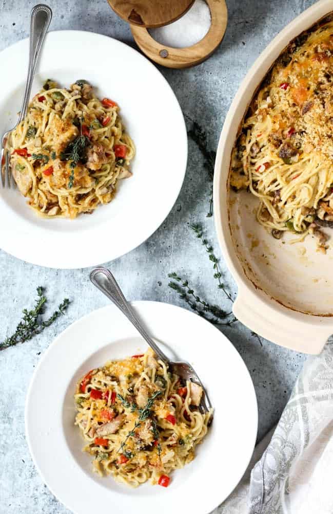 two bowls of Chicken Spaghetti or spaghetti noodles covered in a mushroom cream sauce with chicken, onions and peppers and topped with melted cheddar, breadcrumbs, and crispy jalapenos