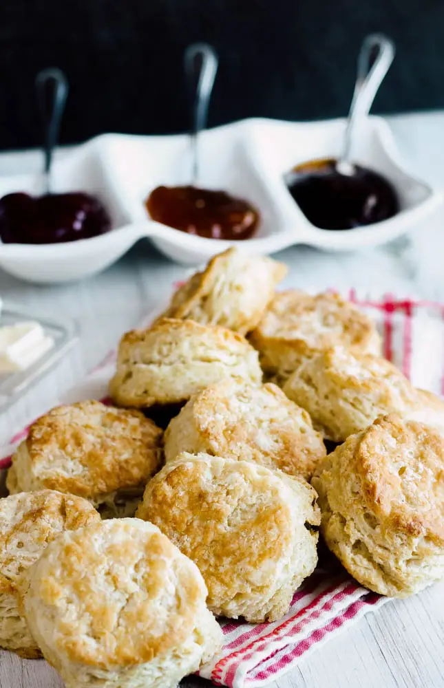 pile of Buttermilk Biscuits on a pink and white linen with three different jams in the background