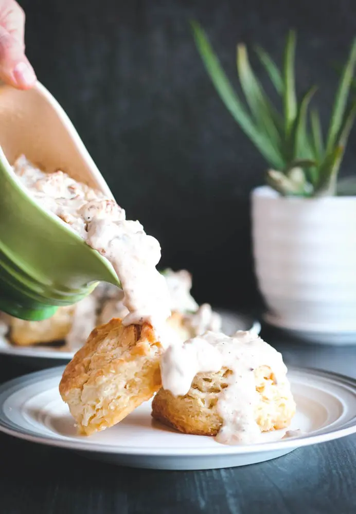 sausage gravy being poured over two buttermilk biscuits