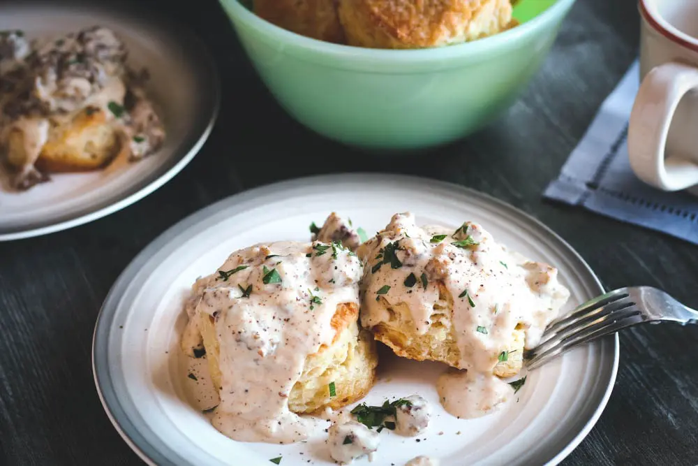 two Buttermilk Biscuits covered in Sausage Gravy on a round white plate