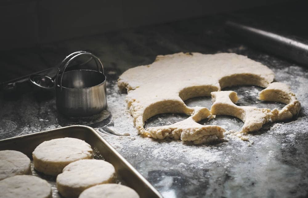 Buttermilk Biscuit dough rolled out on a floured work surface with some biscuits stamped out and placed on a sheet pan