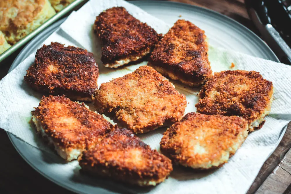 golden brown fried pork chops on a plate with a paper towel to capture excess grease