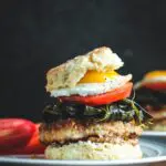 Pork and Collard Greens Biscuit Sandwich with layers of biscuit, whole grain mustard, fried pork chop, cooked collard greens, sliced tomato and a sunny side up egg