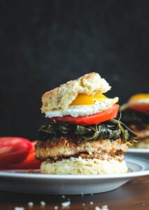 Pork and Collard Greens Biscuit Sandwich with layers of biscuit, whole grain mustard, fried pork chop, cooked collard greens, sliced tomato and a sunny side up egg