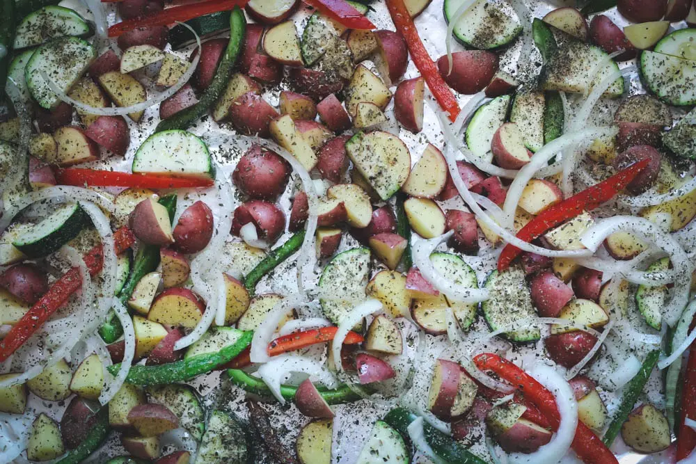 a sheet pan scattered with diced red potatoes and sliced zucchini, green & red bell pepper, and white onion