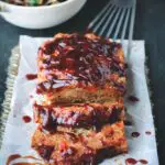 Sausage and Peppers Meatloaf sliced and served on a silver platter with parchment paper and Italian Roasted Vegetables in the background