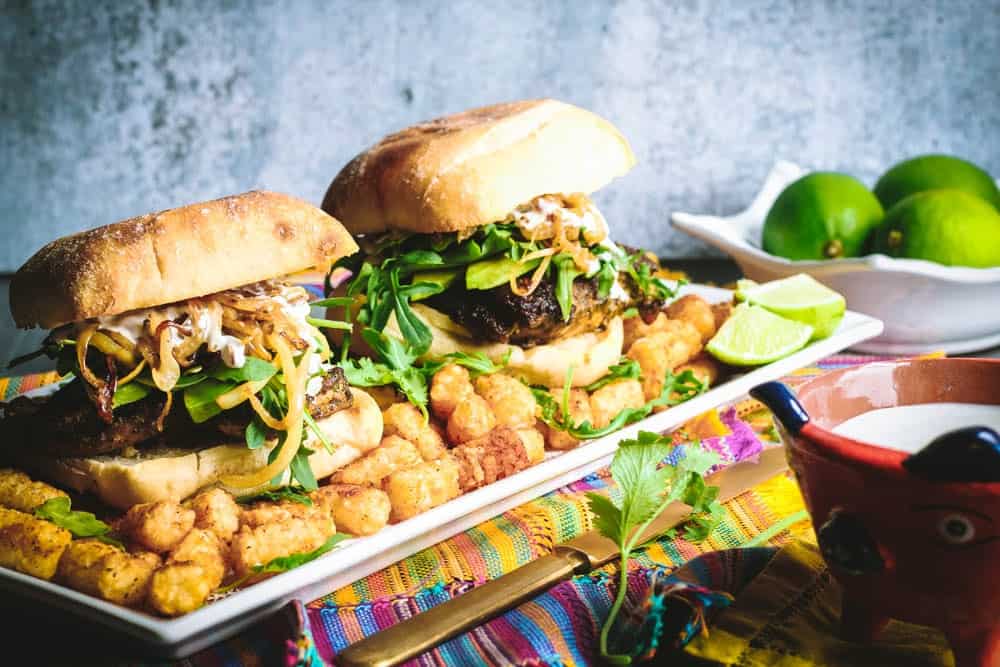 Cilantro Chicken Sandwiches with Chili-Spiced Tater Tots on a long rectangular white plate with a bowl of limes in the background