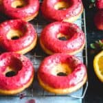 closeup shot of orange donuts with strawberry glaze on a cooling rack with fresh strawberries and oranges