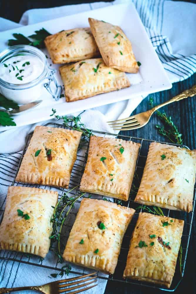closeup of shepherd's hand pies on a cooling rack with one pie split open on a small white plate