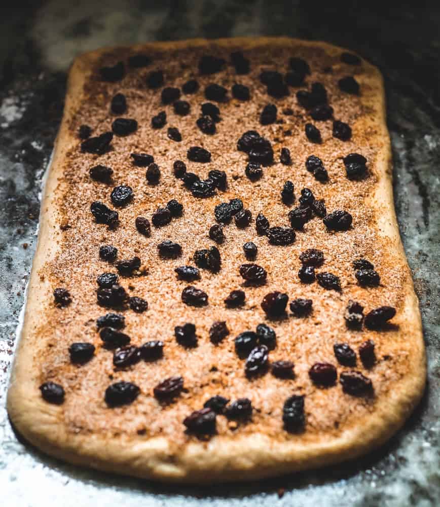 Cinnamon Swirl Bread dough rolled out on a work surface and topped with cinnamon sugar and raisins