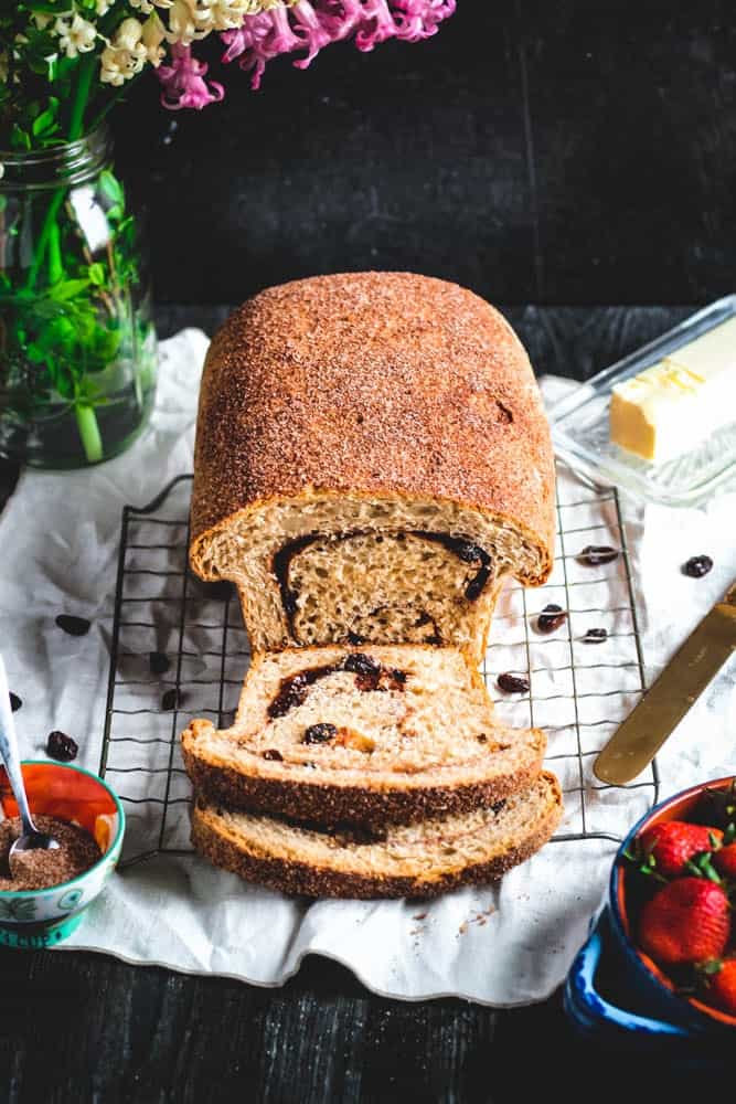 a loaf of cinnamon swirl bread on a wire rack with two slices cut from one end