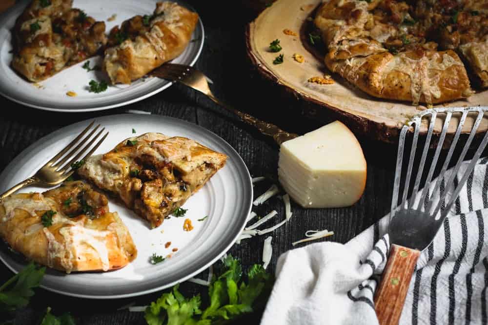 chicken potpie crostata being served from a wooden cutting board with a block of fontina cheese