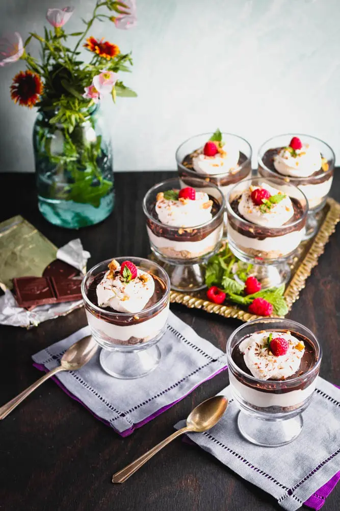 overhead shot of Chocolate Cheesecake Trifles layered in individual trifle dishes served with fresh raspberry and mint as garnish and fresh flowers in the background