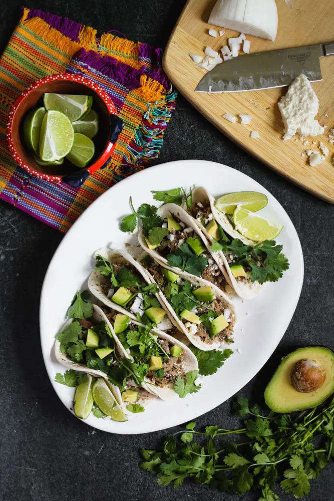 overhead shot of braised salsa verde pork tacos on flour tortillas topped with cilantro and diced avocado