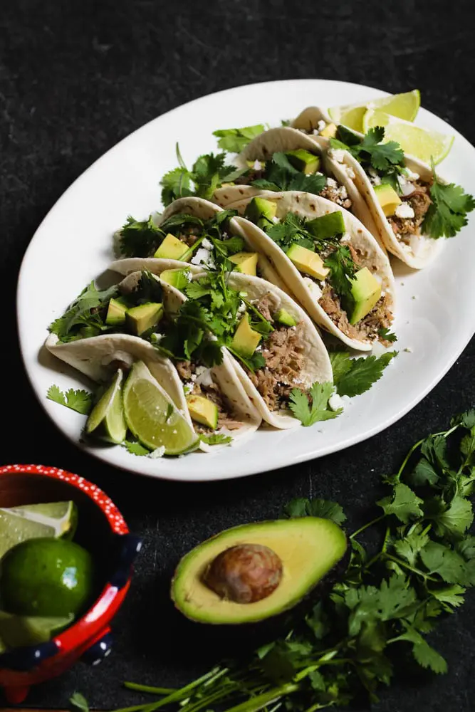 braised salsa verde pork tacos on flour tortillas topped with cilantro and diced avocado