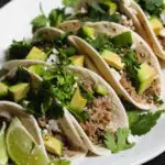 closeup shot of braised salsa verde pork tacos on flour tortillas topped with cilantro and diced avocado