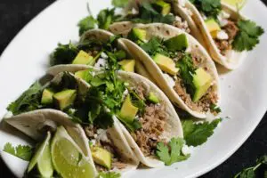 closeup shot of braised salsa verde pork tacos on flour tortillas topped with cilantro and diced avocado