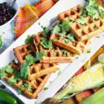 a long rectangular plate of black bean and corn waffles topped with cilantro and a small bowl of black beans on the side