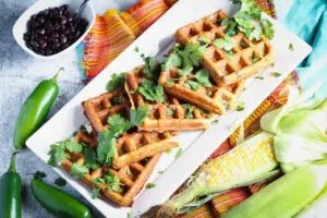 a long rectangular plate of black bean and corn waffles topped with cilantro and a small bowl of black beans on the side