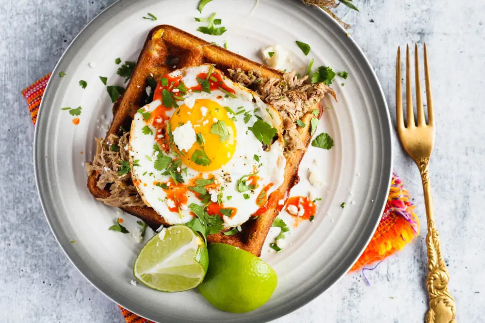 black bean and corn waffle on a small plate topped with a sunny side up egg and cilantro and a side of lime