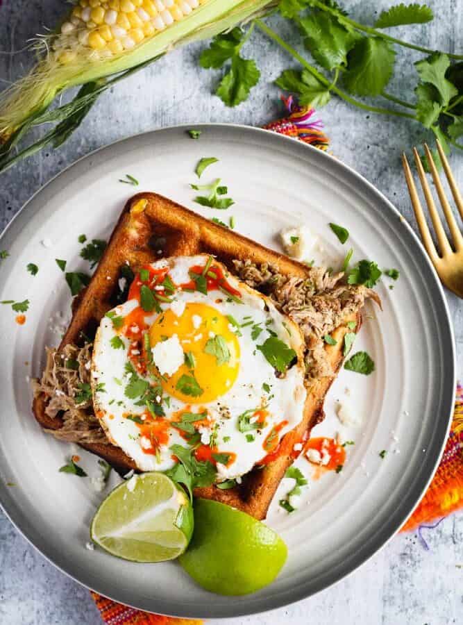 black bean and corn waffle on a small plate topped with a sunny side up egg and cilantro and a side of lime