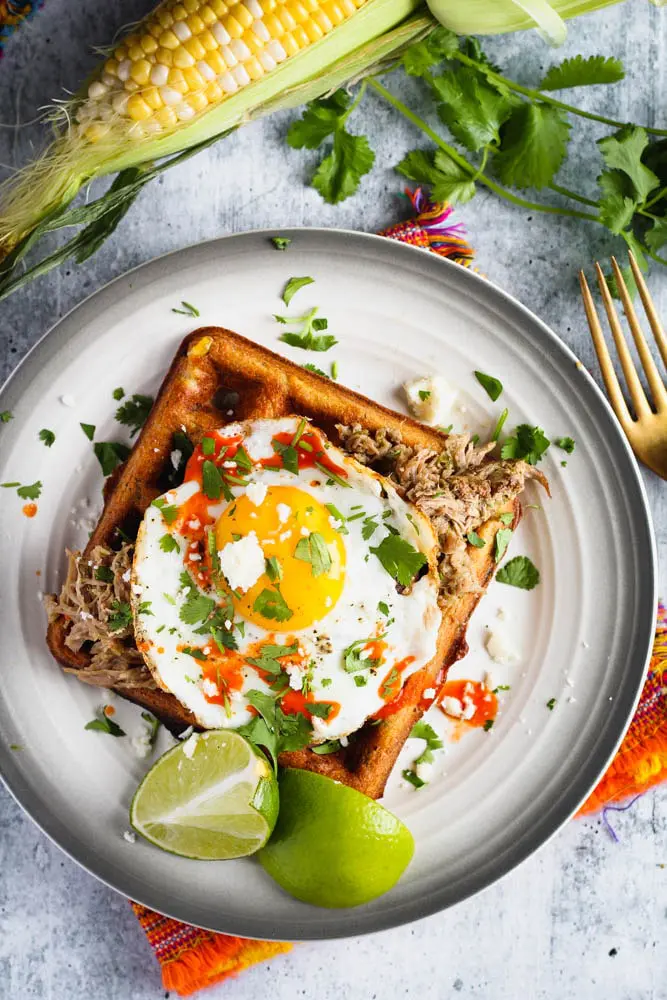 black bean and corn waffle on a small plate topped with a sunny side up egg and cilantro and a side of lime